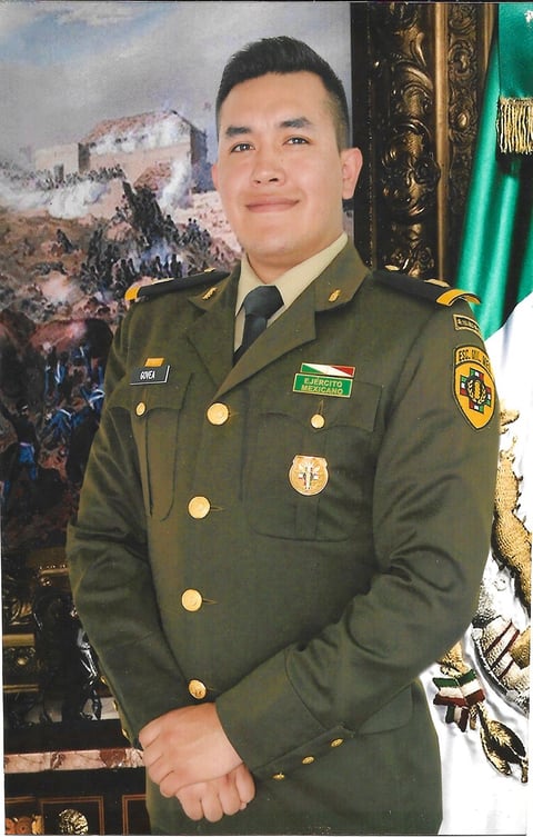 Military officer in olive green uniform with medals and insignia standing in formal portrait pose