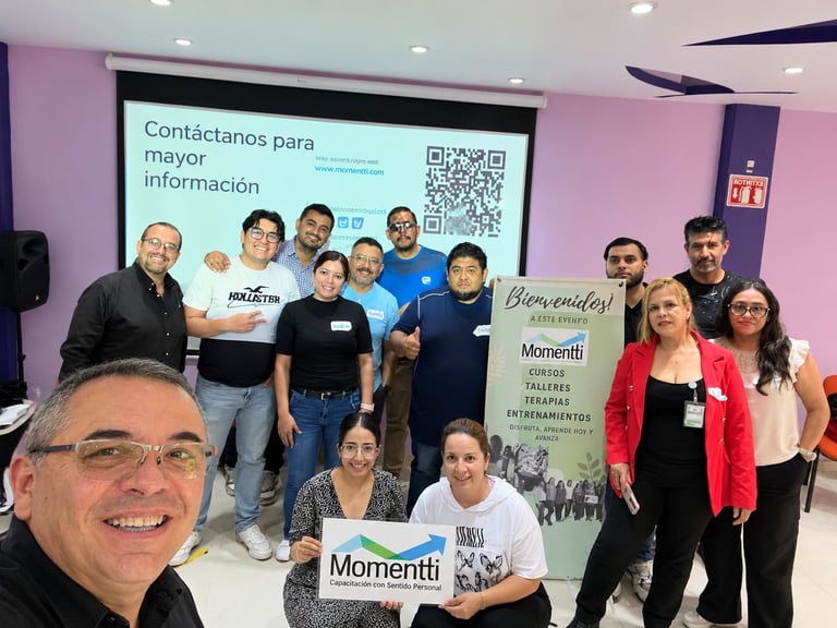 Group photo of diverse team members smiling at camera with Momentti branding and projection screen displaying Spanish text in background