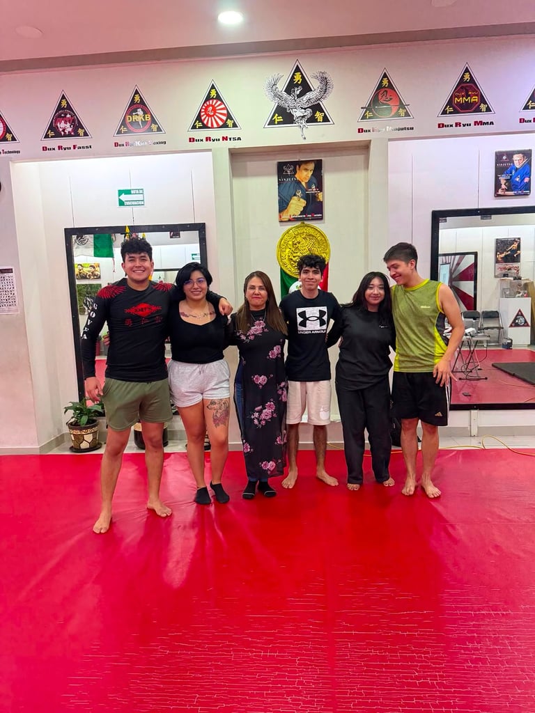 Six people standing together on a red mat in a martial arts studio with triangular emblems and posters on the wall