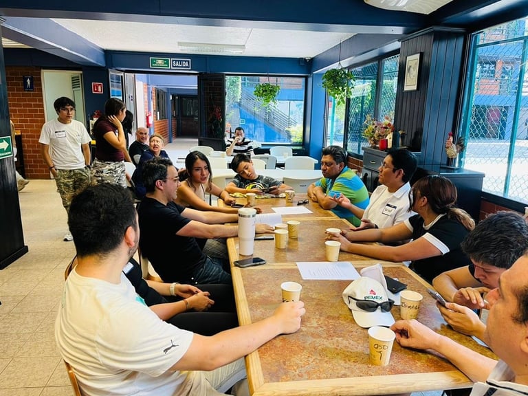 Group of people gathered around wooden tables in a modern office space with blue walls and large windows, eating and socializing together