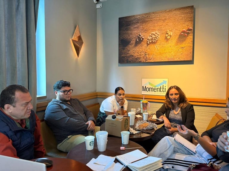 Four people sitting around a table in a meeting room with artwork on walls and papers and drinks on the table