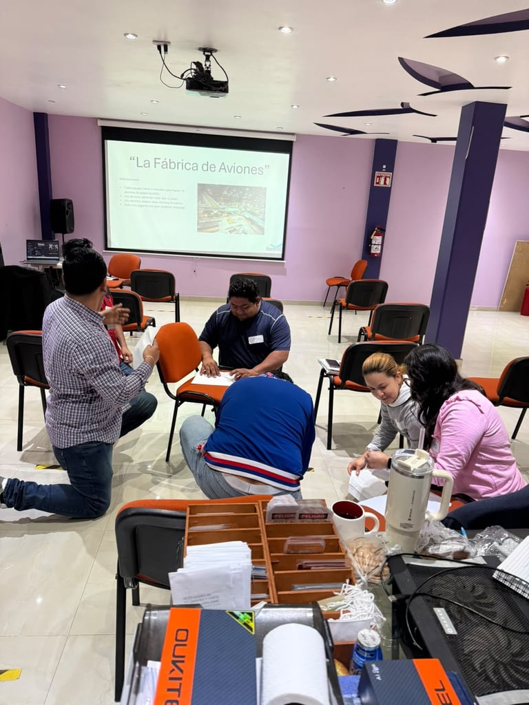 Group of people participating in a workshop in a purple room with a presentation screen showing La Fabrica de Aviones displayed on the wall.
